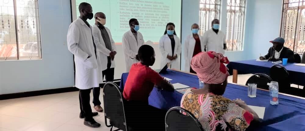 A group of healthcare professionals and facilitators standing in front of participants during the mental health awareness event conducted at Kilombero Sugar Company in Ifakara, Tanzania.